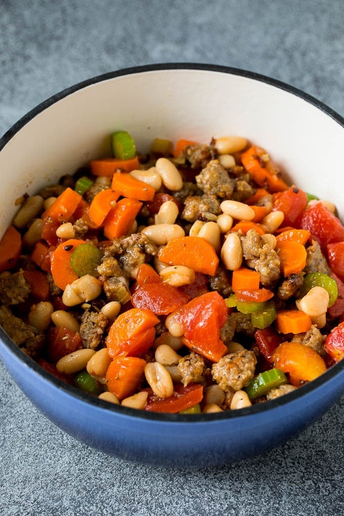 This Tuscan white bean soup is a hearty blend of Italian sausage, vegetables and beans, all simmered together in a savory tomato broth. A mixture of beans, tomatoes, vegetables and sausage in a pot.