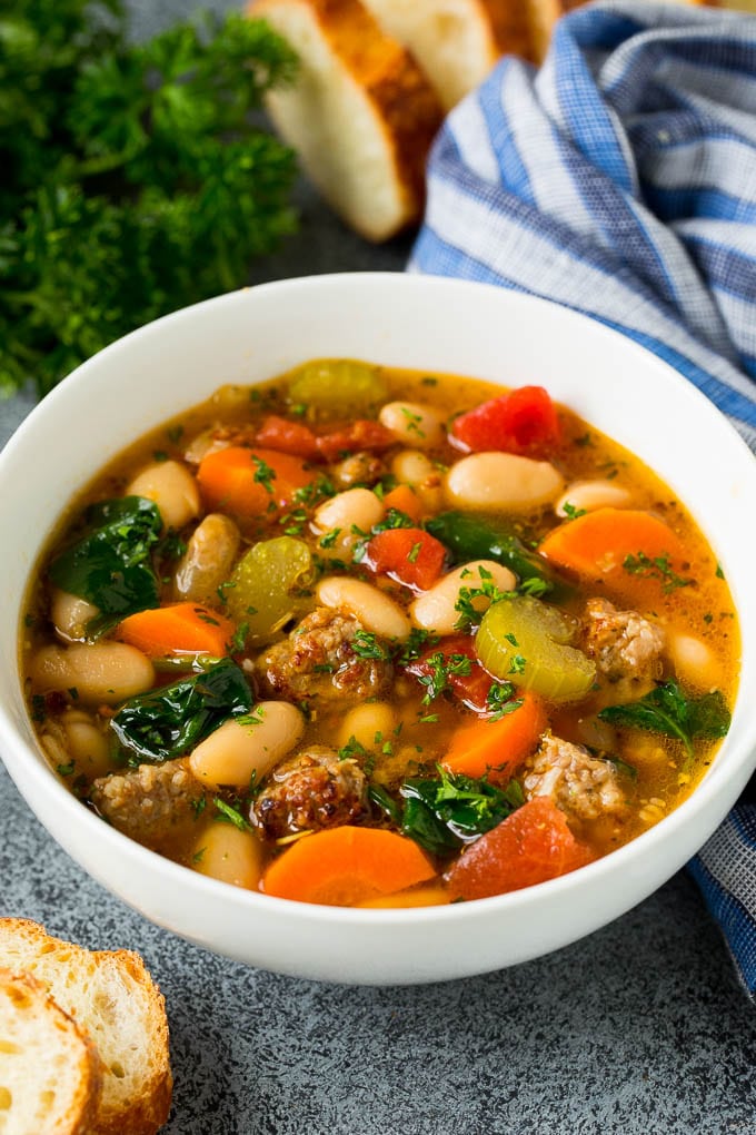 This Tuscan white bean soup is a hearty blend of Italian sausage, vegetables and beans, all simmered together in a savory tomato broth. A bowl of white bean soup with Italian sausage, tomatoes and spinach.
