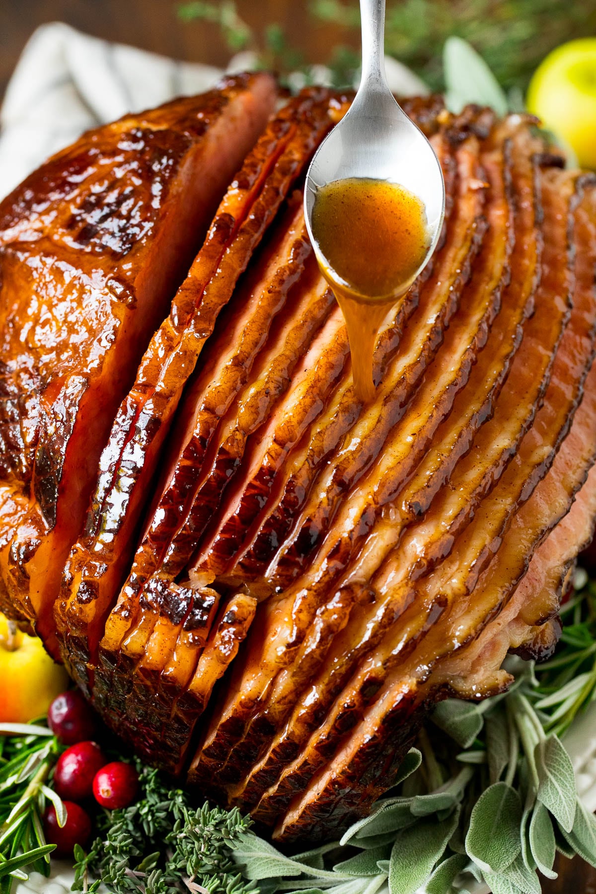 This ham glaze is a combination of butter, brown sugar, pineapple juice and spices, all simmered together until thickened. A spoon pouring ham glaze over a ham.