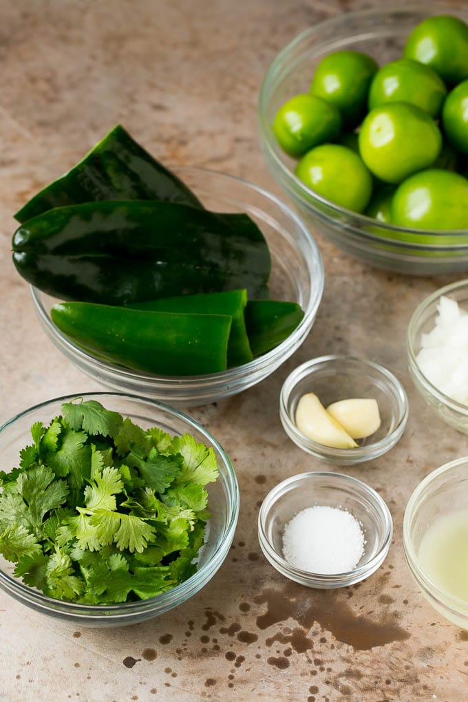 This homemade salsa verde is a combination of roasted chilies, tomatillos, garlic, cilantro and lime juice, all blended together to make a light and refreshing dip. Bowls of tomatillos, peppers, garlic, cilantro and seasonings.