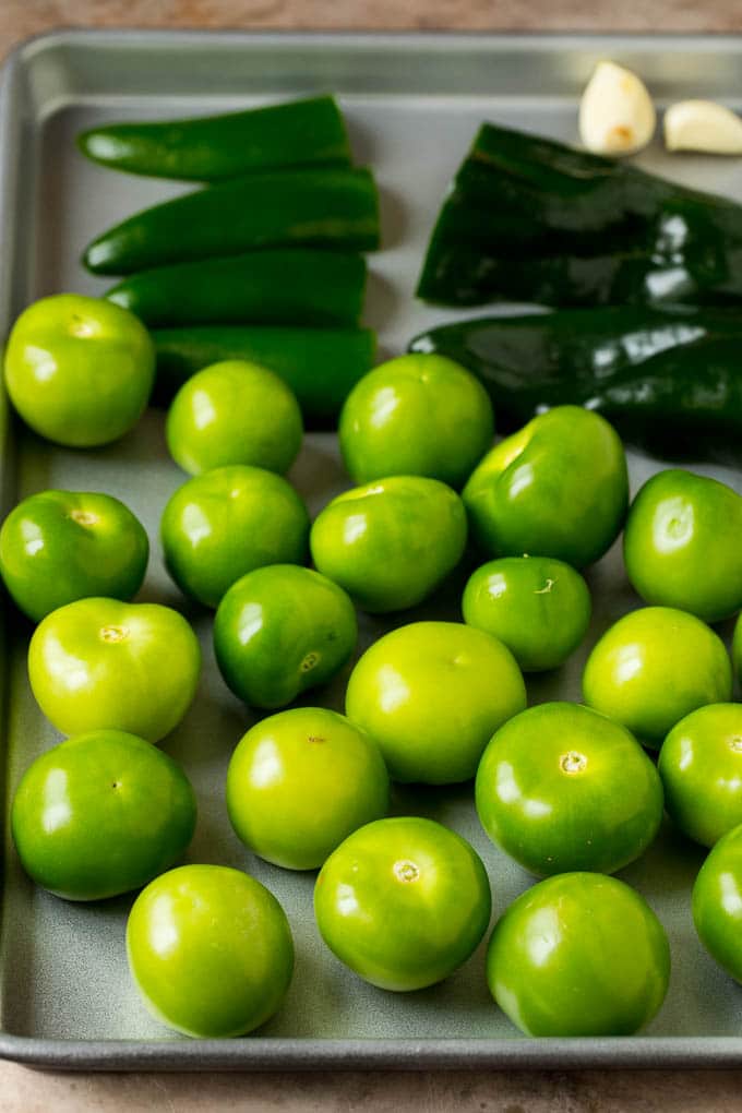 This homemade salsa verde is a combination of roasted chilies, tomatillos, garlic, cilantro and lime juice, all blended together to make a light and refreshing dip. Tomatillos and halved peppers on a sheet pan.