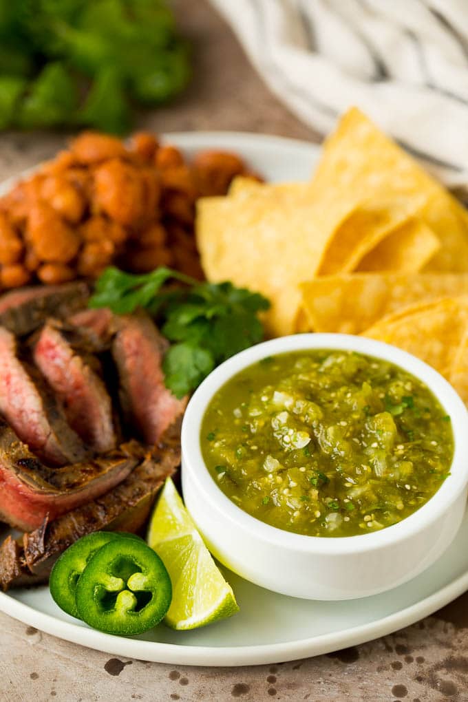 This homemade salsa verde is a combination of roasted chilies, tomatillos, garlic, cilantro and lime juice, all blended together to make a light and refreshing dip. Salsa verde served with carne asada, beans and tortillas.