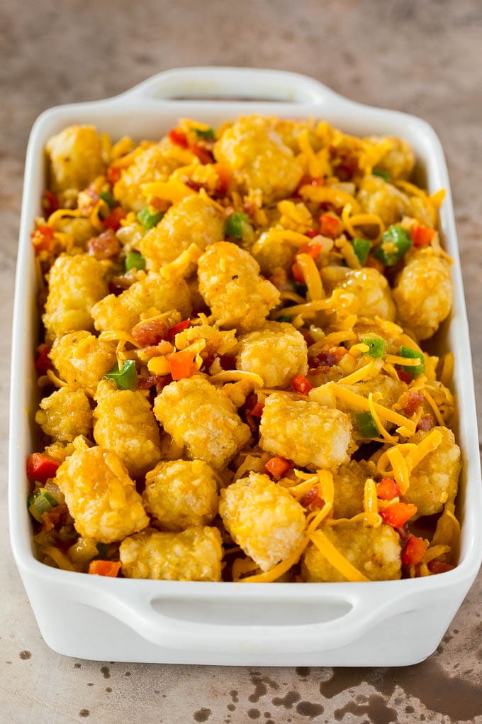 This tater tot breakfast casserole is made with bacon, eggs, veggies, potato tots and plenty of cheese, all baked together to make a hearty meal. Potato tots mixed with eggs, bacon and cheese in a baking dish.