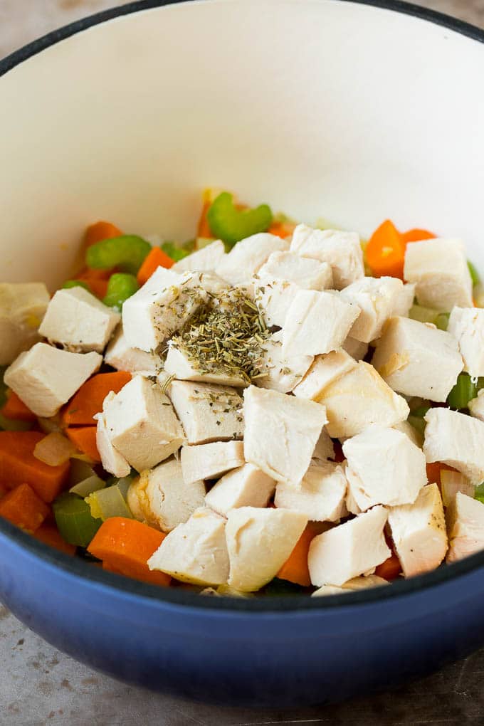 This matzo ball soup is chicken and vegetables simmered with matzo balls in a savory broth with fresh herbs. Diced chicken and herbs in a pot with vegetables.