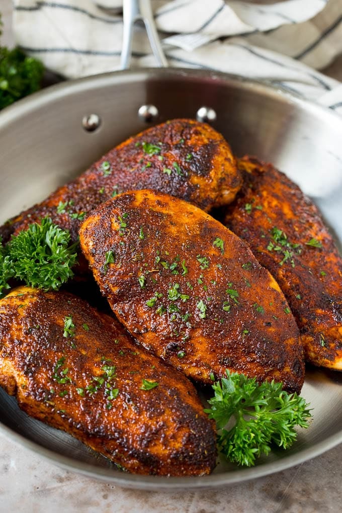 A pan of blackened chicken breasts garnished with fresh parsley.