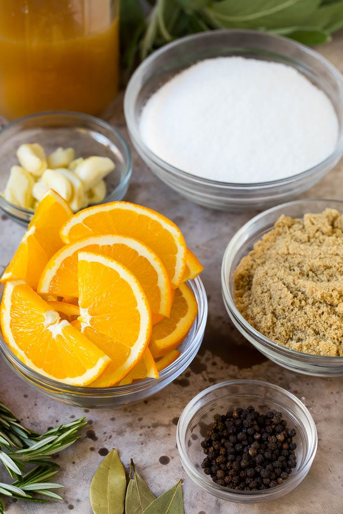 This is a complete guide on how to brine a turkey to get the most tender and flavorful bird each and every time. Bowls of ingredients including orange slices, brown sugar, garlic, herbs and seasonings.