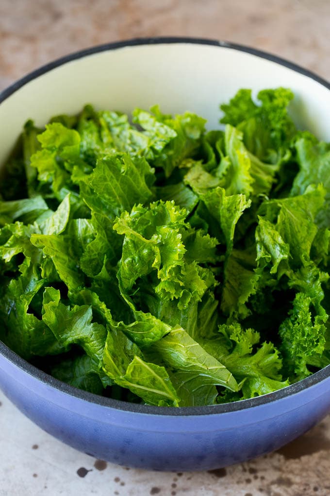 These Southern style mustard greens are cooked with smoky bacon and seasonings until tender and flavorful. Torn leafy vegetables in a pot with bacon and onions.