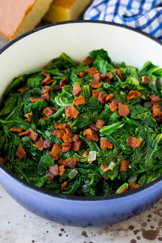 These Southern style mustard greens are cooked with smoky bacon and seasonings until tender and flavorful. A pot of mustard greens topped with bacon.