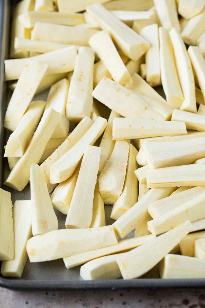 These roasted parsnips are coated in garlic, olive oil and herbs, then cooked in the oven until golden brown and tender. A quick and easy side dish option that pairs perfectly with chicken, beef and pork. Parsnips cut into sticks on a sheet pan.