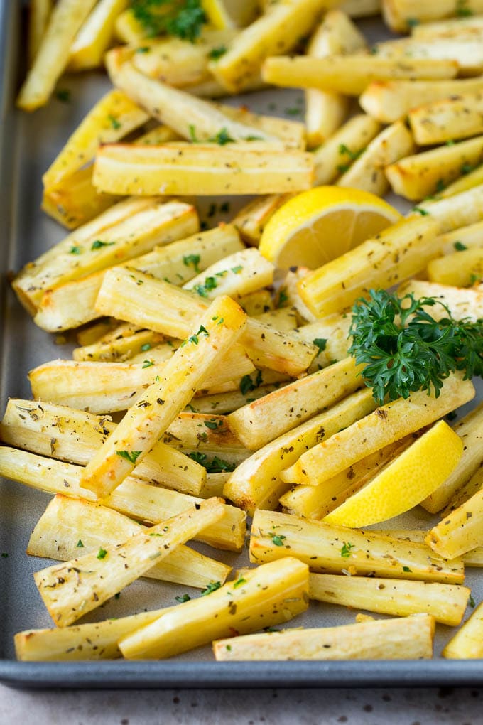 These roasted parsnips are coated in garlic, olive oil and herbs, then cooked in the oven until golden brown and tender. A quick and easy side dish option that pairs perfectly with chicken, beef and pork. A sheet pan of roasted parsnips garnished with fresh parsley.