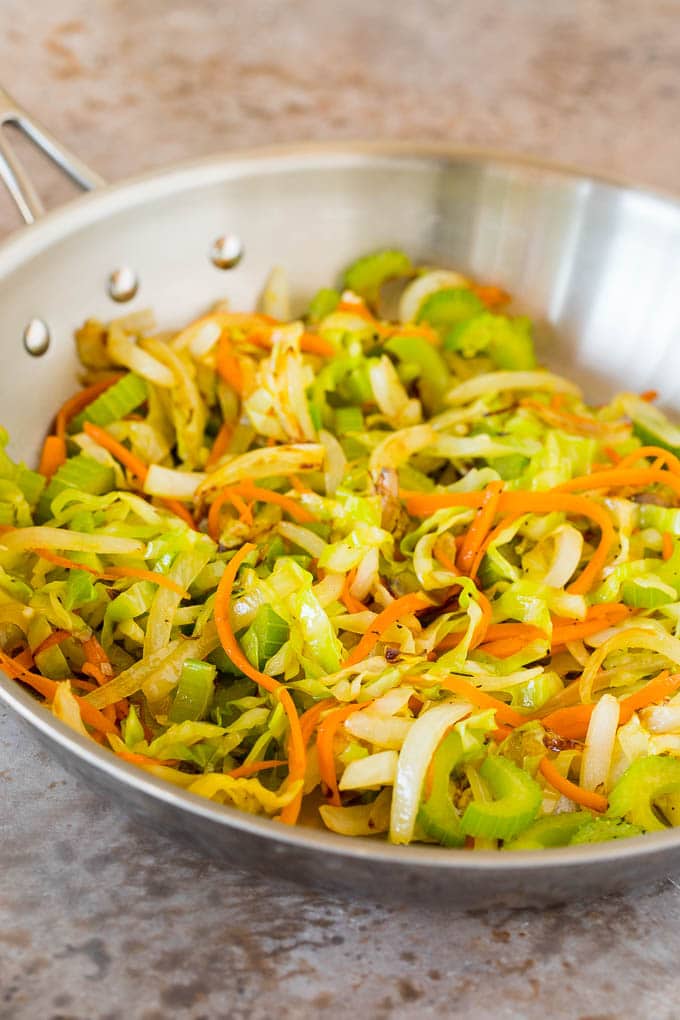 This shrimp lo mein is succulent shrimp with vegetables and egg noodles, all tossed together in a savory sauce. Sauteed cabbage, carrots and onions in a pan.