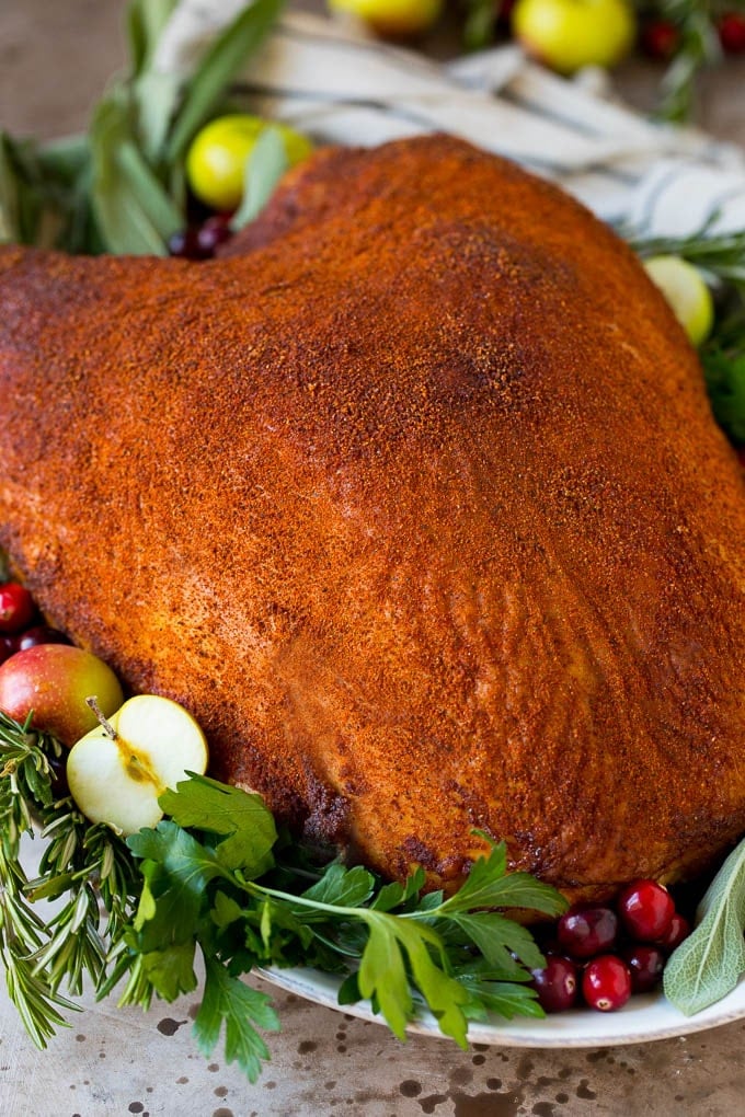 This smoked turkey breast is soaked in brine, then coated in homemade spice rub and cooked on a smoker until it is tender and juicy. A smoked turkey breast on a platter garnished with fruit and herbs.