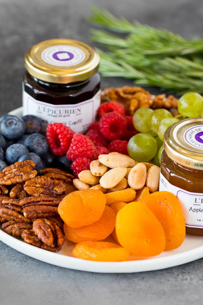 A guide to creating the best cheese board with a variety of different cheeses, crackers, fruit and accompaniments. A plate with fresh and dried fruit, nuts and jam.