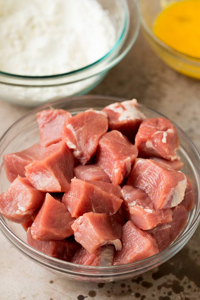 This sweet and sour pork is chunks of pork tenderloin that are breaded and fried, then tossed with pineapple and fresh vegetables in a homemade sauce. Cubes of pork tenderloin, a bowl of flour and a bowl of eggs.