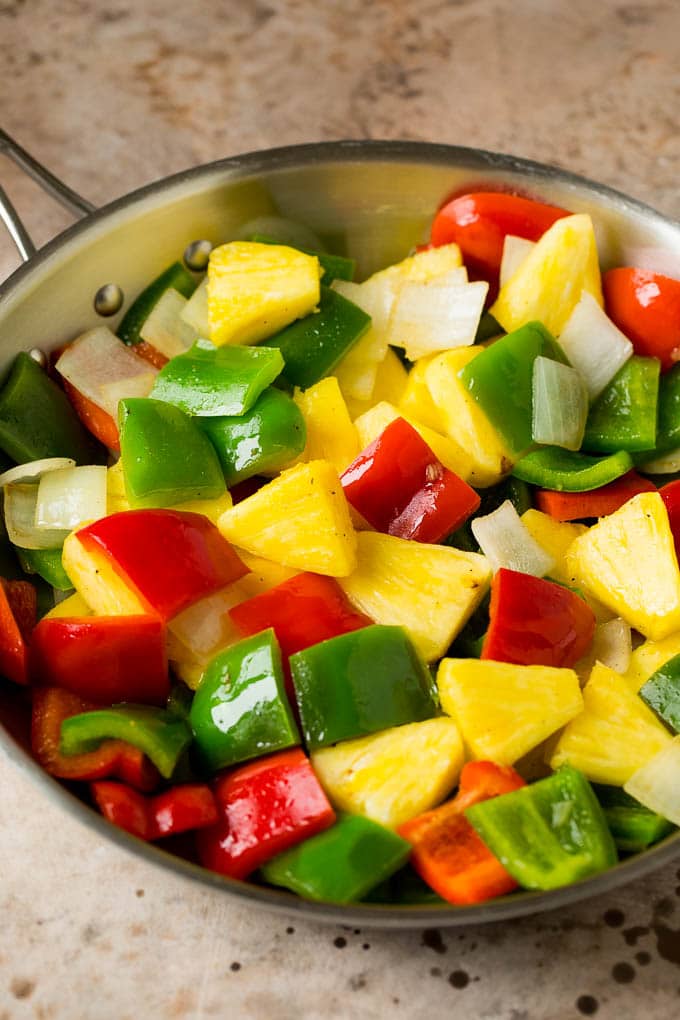 This sweet and sour pork is chunks of pork tenderloin that are breaded and fried, then tossed with pineapple and fresh vegetables in a homemade sauce. Pineapple, bell peppers and onions in a pan.