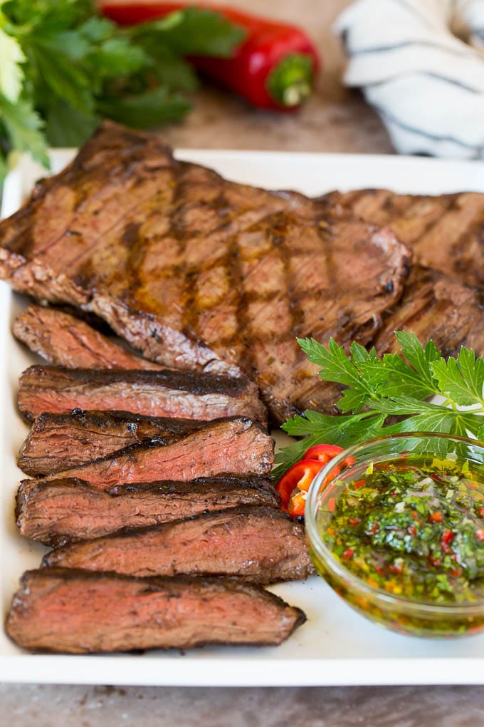 This churrasco recipe is marinated skirt steak that is grilled to tender perfection, then topped with a fresh and flavorful chimichurri sauce. Sliced churrasco served with a bowl of chimichurri sauce.