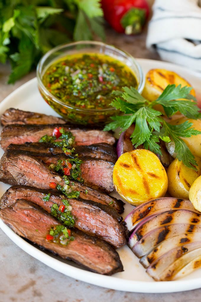 This churrasco recipe is marinated skirt steak that is grilled to tender perfection, then topped with a fresh and flavorful chimichurri sauce. Churrasco on a plate with chimichurri sauce and grilled vegetables.