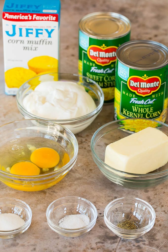 This cornbread casserole is a blend of corn muffin mix, canned corn, creamed corn, seasoning, eggs and butter, all baked together to make a hearty side dish. Bowls of ingredients with cans of corn and a box of corn muffin mix.