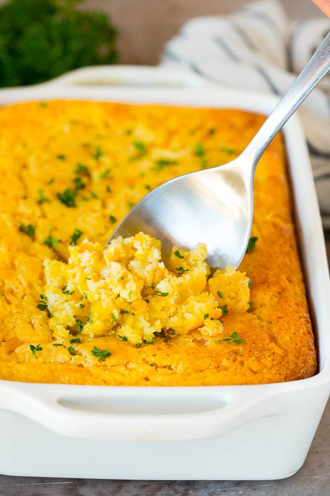 This cornbread casserole is a blend of corn muffin mix, canned corn, creamed corn, seasoning, eggs and butter, all baked together to make a hearty side dish. Cornbread casserole with a serving spoon in it.