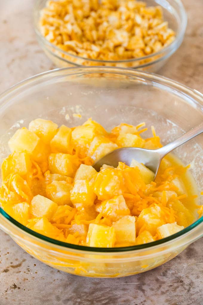 This Southern pineapple casserole is pineapple, cheese and buttery crackers, all baked together to create a sweet and savory side dish. A bowl of pineapple chunks mixed with cheddar cheese, flour and sugar.