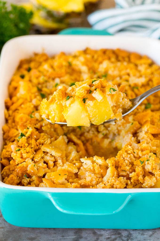 This Southern pineapple casserole is pineapple, cheese and buttery crackers, all baked together to create a sweet and savory side dish. A spoon holding a serving of pineapple casserole topped with crackers and parsley.