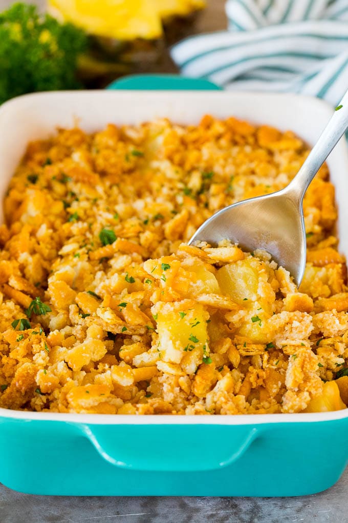 This Southern pineapple casserole is pineapple, cheese and buttery crackers, all baked together to create a sweet and savory side dish. A serving spoon in a dish of pineapple casserole.