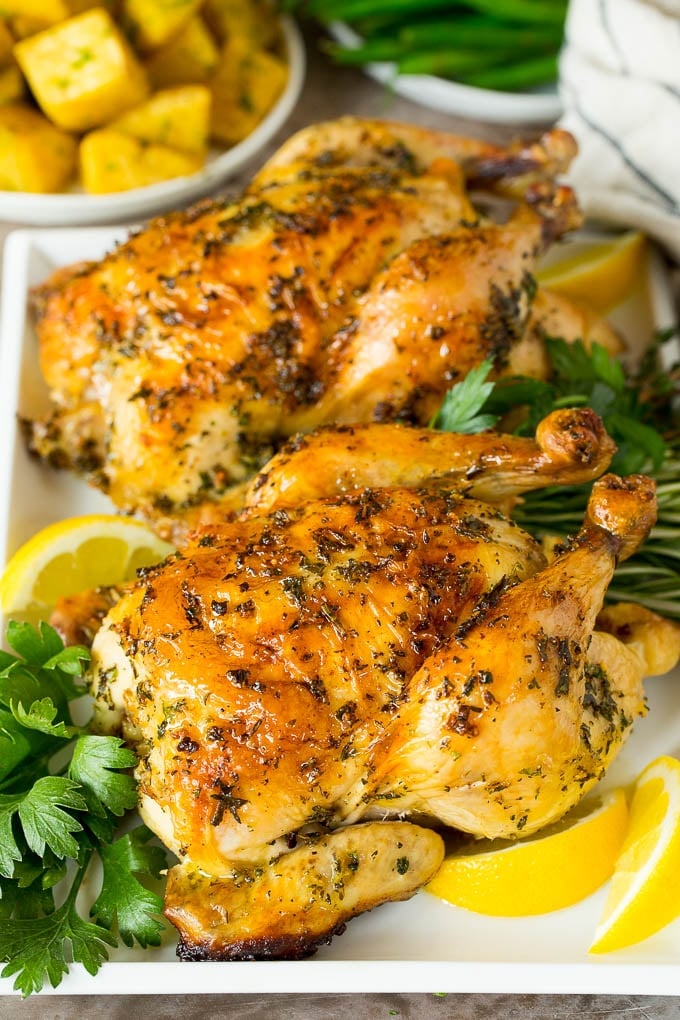 This roasted Cornish hen recipe is an easy and elegant way to make a meal that's quick enough for a busy weeknight, yet fancy enough for a special occasion. Roasted cornish hen on a serving tray garnished with herbs and lemon.
