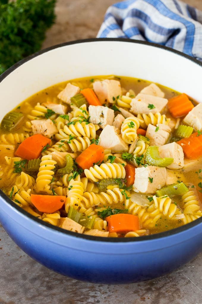 This turkey noodle soup is chunks of turkey, vegetables and pasta, all simmered together in a homemade broth. A pot of turkey noodle soup with vegetables, garnished with parsley.