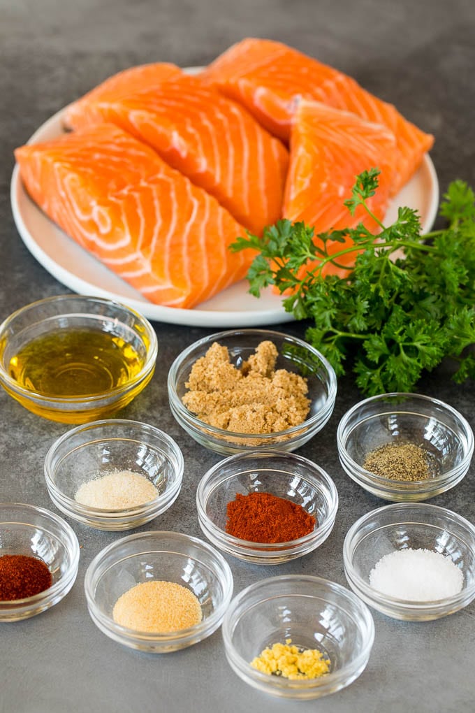 This air fryer salmon is fresh fish fillets topped with a homemade spice rub, then cooked to golden brown perfection. Salmon fillets and bowls of herbs, spices and olive oil.