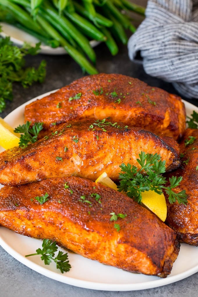 This air fryer salmon is fresh fish fillets topped with a homemade spice rub, then cooked to golden brown perfection. A plate of air fryer salmon fillets garnished with lemon and herbs.
