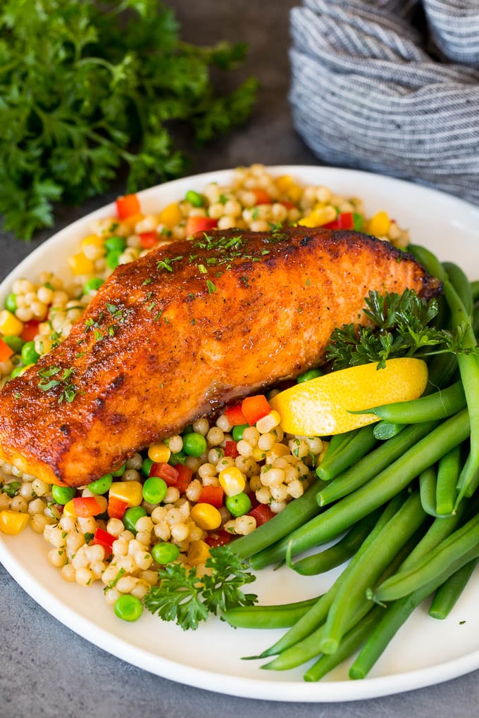 This air fryer salmon is fresh fish fillets topped with a homemade spice rub, then cooked to golden brown perfection. A piece of air fryer salmon served with couscous and green