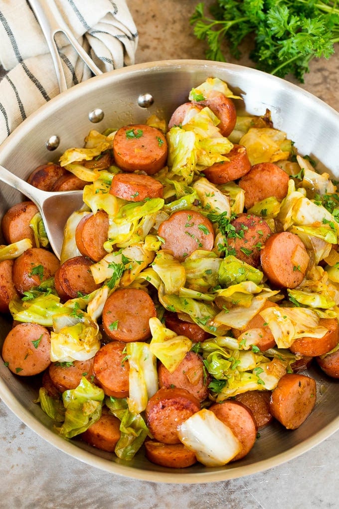 This cabbage and sausage skillet is a combination of smoked sausage, vegetables and savory seasonings, all cooked together to make a quick and easy dinner. A pan of cabbage and sausage with parsley and a serving spoon.