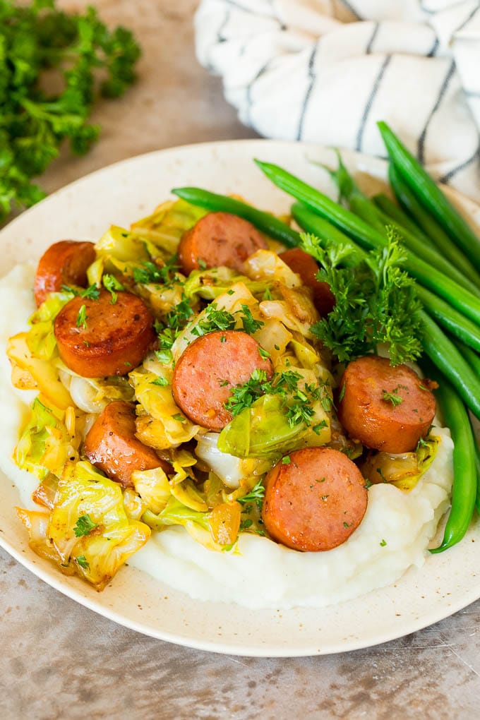 This cabbage and sausage skillet is a combination of smoked sausage, vegetables and savory seasonings, all cooked together to make a quick and easy dinner. A plate of cabbage and sausage served over mashed potatoes with green beans.