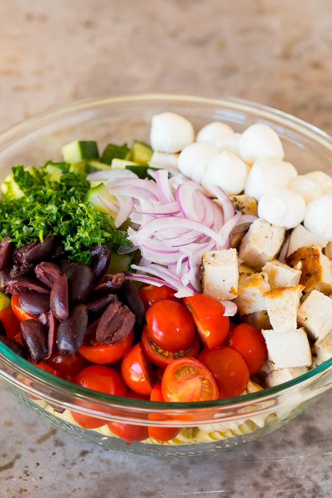This chicken pasta salad is grilled chicken with olives, cheese and fresh vegetables, all tossed in a homemade Italian dressing. Chicken, vegetables and olives in a bowl with pasta.
