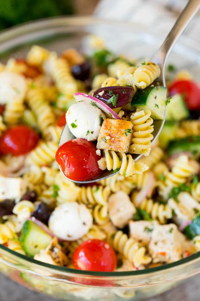 This chicken pasta salad is grilled chicken with olives, cheese and fresh vegetables, all tossed in a homemade Italian dressing. A spoon holding up a serving of chicken pasta salad.