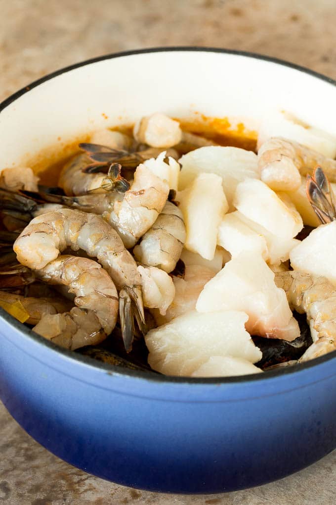 This bouillabaisse is French seafood stew with fresh fish, shrimp, clams and mussels, all simmered together in a flavorful broth. A pot with broth, fish and shrimp in it.