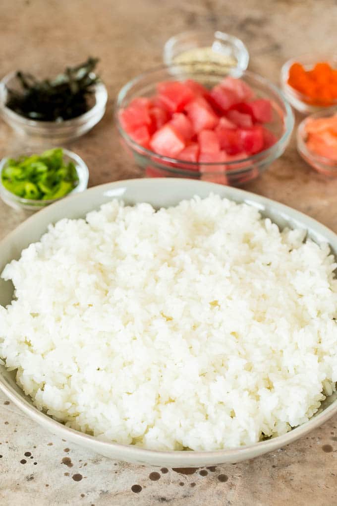 This sushi bowl recipe is assorted fresh fish, avocado, cucumber and seaweed, all served over rice with spicy mayo, picked ginger and tobiko. A bowl of sushi rice with bowls of toppings around it.