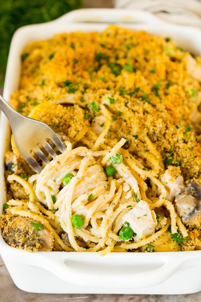 This turkey tetrazzini contains diced turkey, mushrooms and peas, all tossed with pasta in a creamy sauce, then baked to perfection. A fork serving up a portion of turkey tetrazzini.