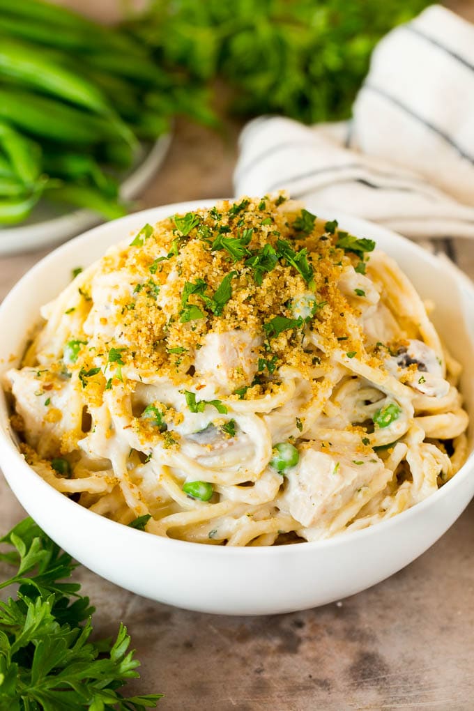 This turkey tetrazzini contains diced turkey, mushrooms and peas, all tossed with pasta in a creamy sauce, then baked to perfection. A bowl of turkey tetrazzini topped with breadcrumbs.