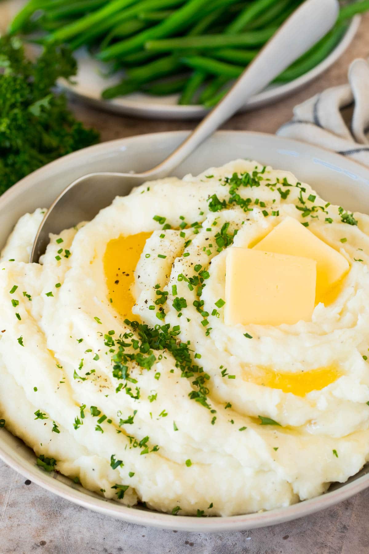 These make ahead mashed potatoes are Russet potatoes that are boiled until tender, then combined with butter, garlic, cream cheese and seasonings to make the ultimate side dish. A bowl of make ahead mashed potatoes topped with butter and herbs.