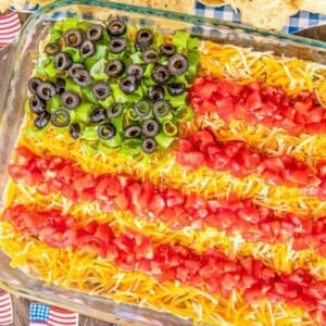 An image of taco dip decorated with tomatoes, cheese and olives to look like an American flag.