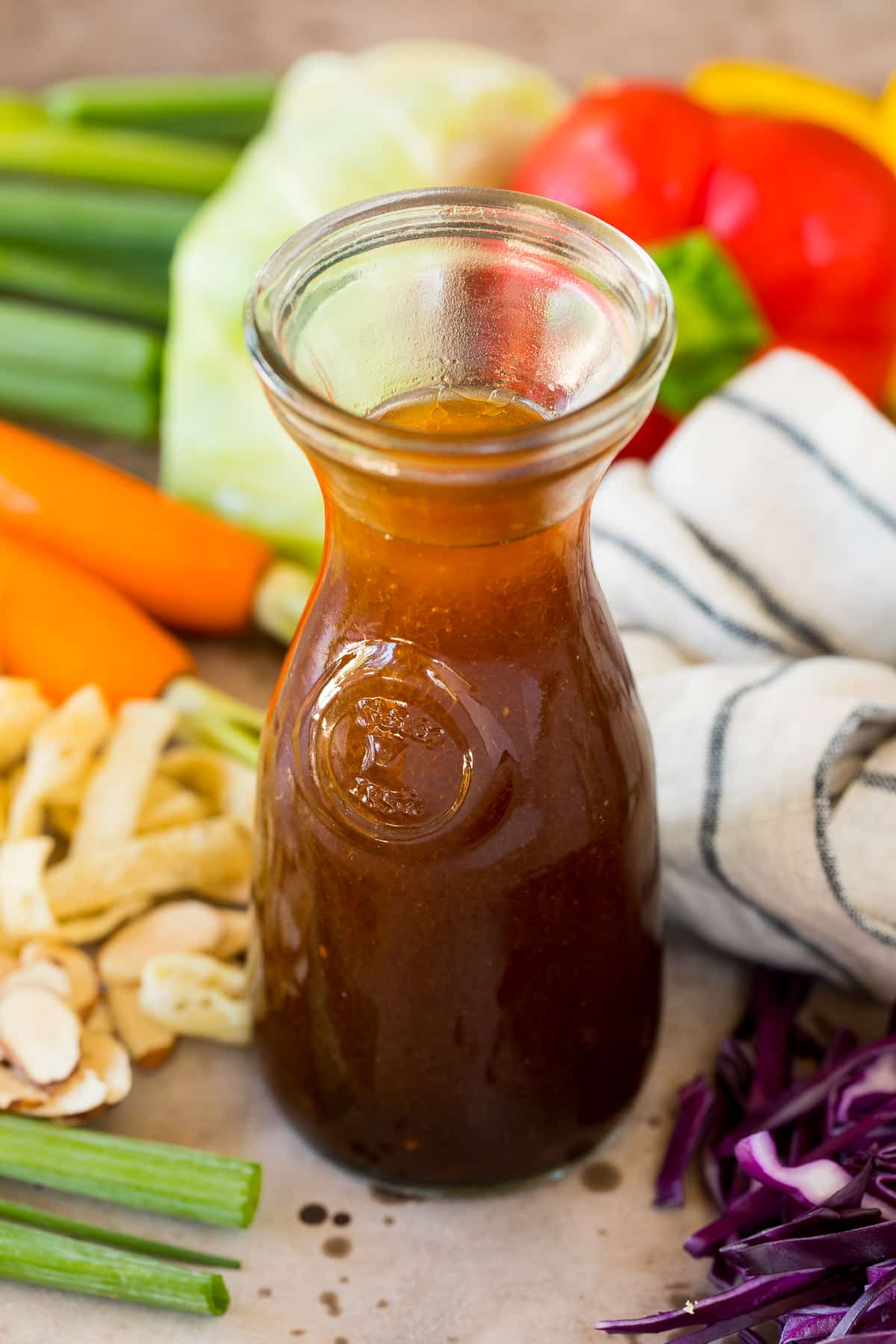 A jar of Asian salad dressing surrounded by vegetables.