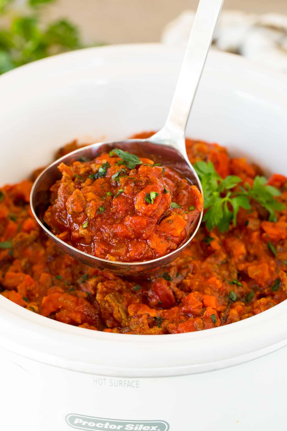 A ladle holding up a serving of slow cooker bolognese sauce.