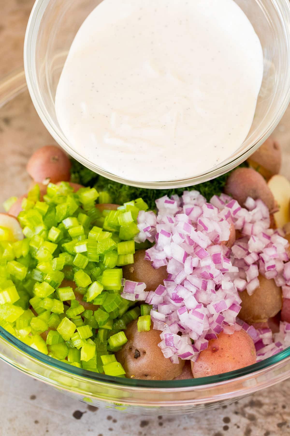 Dressing being poured over potatoes and vegetables.