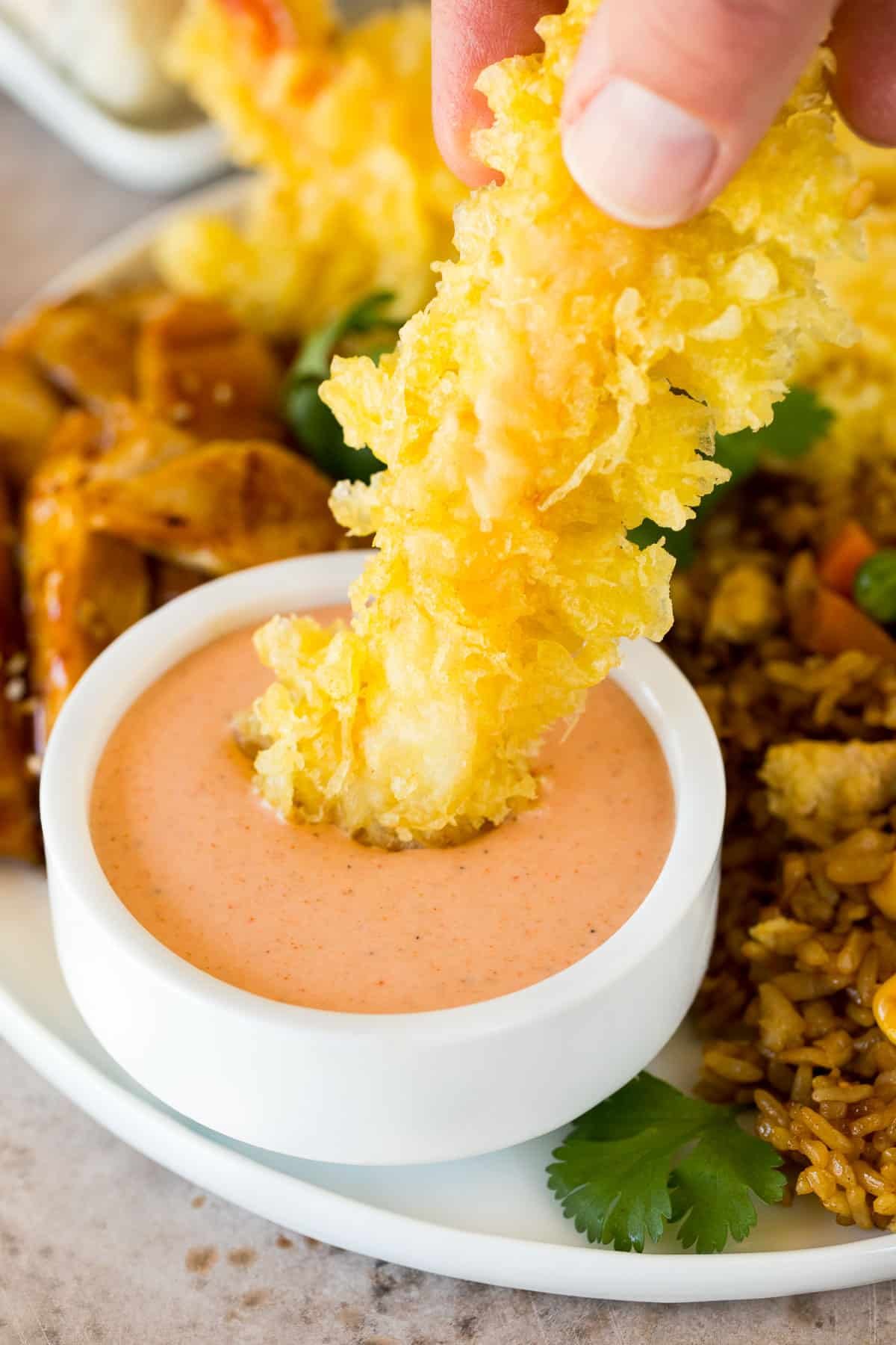 A hand dipping a tempura shrimp into yum yum sauce.