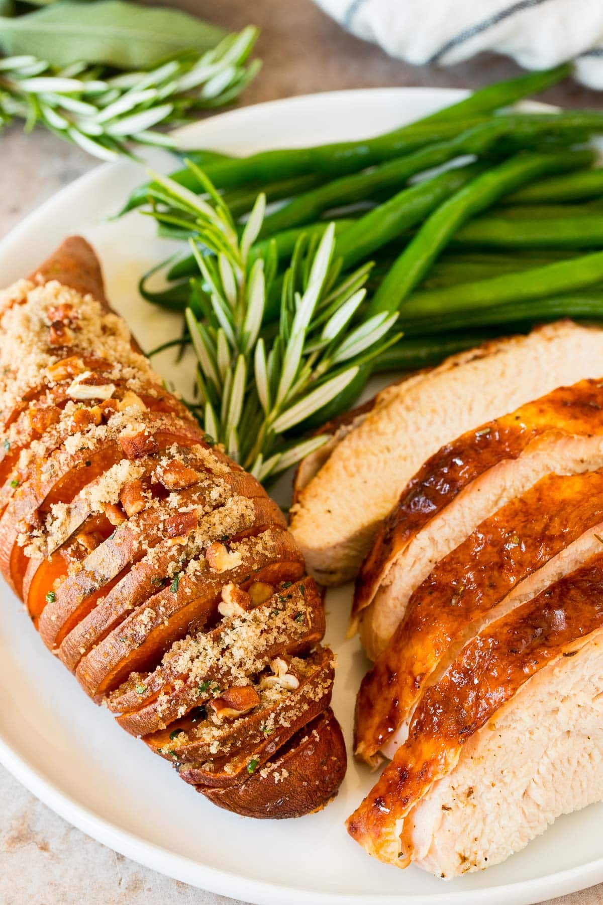 A Hasselback sweet potato on a plate with turkey and green beans.
