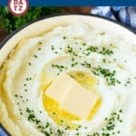 A pot of cream cheese mashed potatoes with, butter, cracked pepper and chives on top.