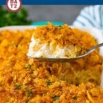 A serving spoon of funeral potatoes served out of a baking dish.
