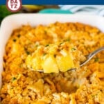 Pineapple casserole being scooped out of a baking dish by a metal spoon.