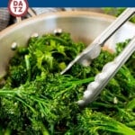 A metal pan with sauteed broccolini and a pair of tongs.